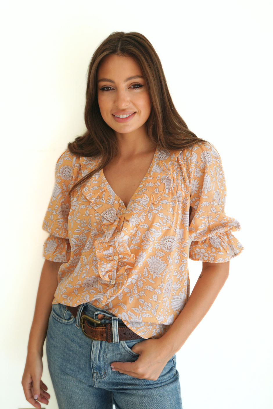 Light Orange Floral Spring/Summer Chloe Shirt from Paneros Clothing with button-up front and Elbow-length sleeves and ruffles. Sustainable cotton fully-lined top with smocking. Front View tucked into denim.