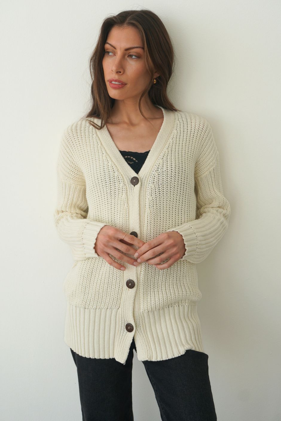 Creamy Off-White Sustainable Cotton Hip-Length Button-up Emily Cardigan by Paneros Clothing. Hand-knitted, slightly oversized cardigan with real coconut shell buttons and ribbed detailing. Front View buttoned.