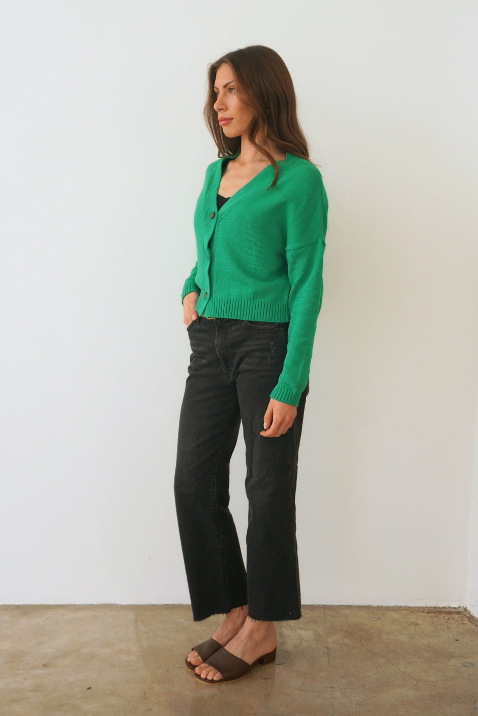 Emerald Green sustainable cropped-length Cotton Diana Cardigan from Paneros Clothing with real coconut shell button-up front, Full sleeves, and feminine handknittting. Side view buttoned.