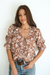 Brown Floral Spring/Summer Chloe Shirt from Paneros Clothing with button-up front and Elbow-length sleeves and ruffles. Sustainable cotton fully-lined top with smocking. Front View tucked into denim.