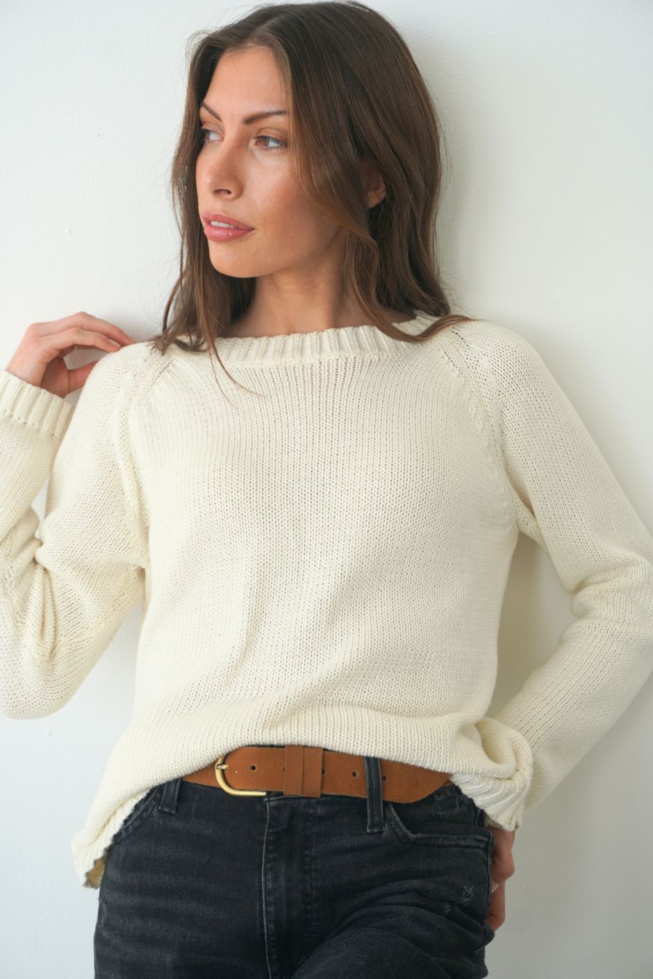 Creamy Off-White sustainable cotton handknitted Sloane Crewneck by Paneros Clothing. Relaxed-fit hip-length crewneck sweater with long sleeves and ribbing details. Front View tucked into denim.