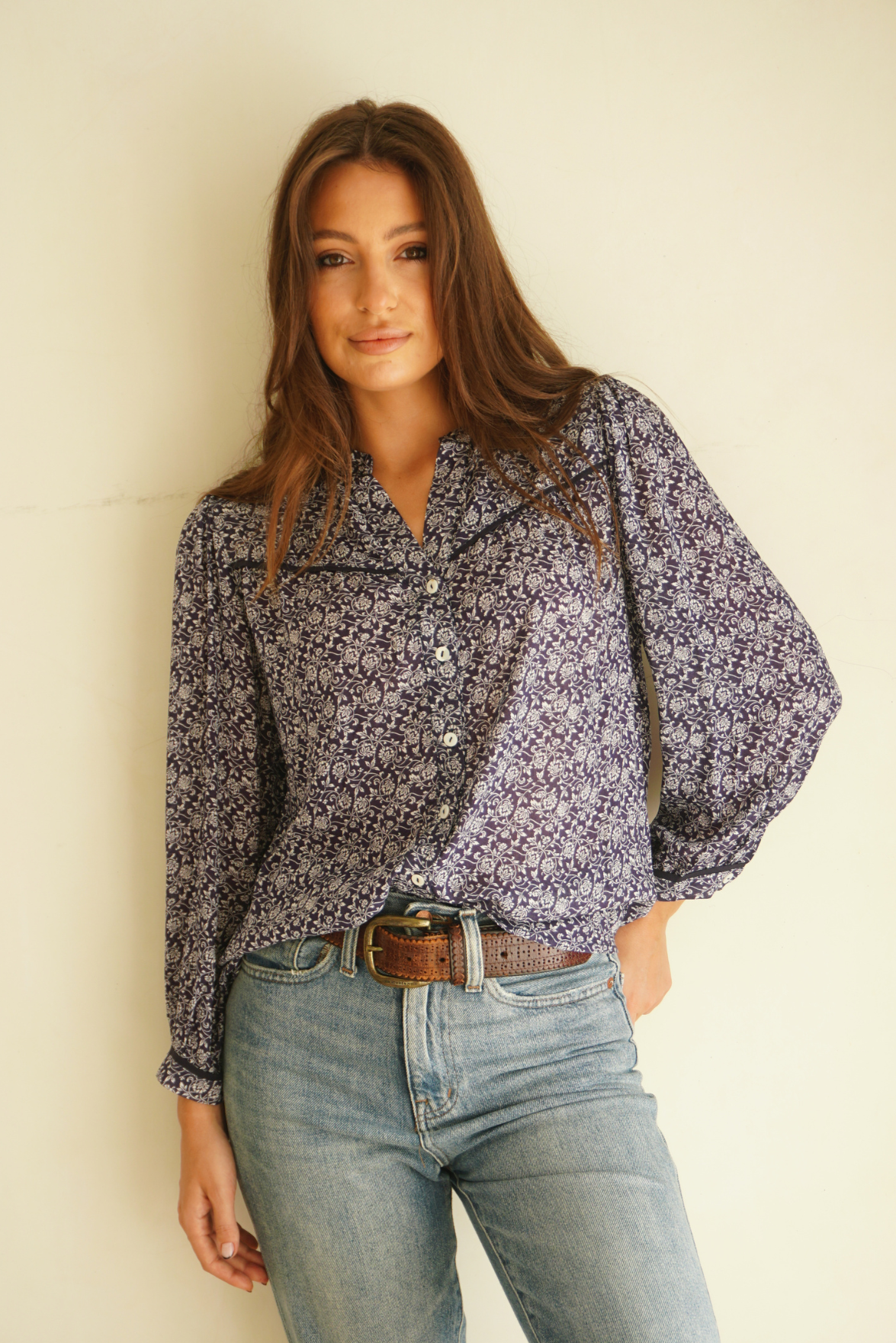 Blue Floral Print Anna Shirt from Paneros Clothing with button-up front and long sleeves. Sustainable rayon dobby shirt blouse in blue floral print with contrast navy piping details. Front View tucked into denim.