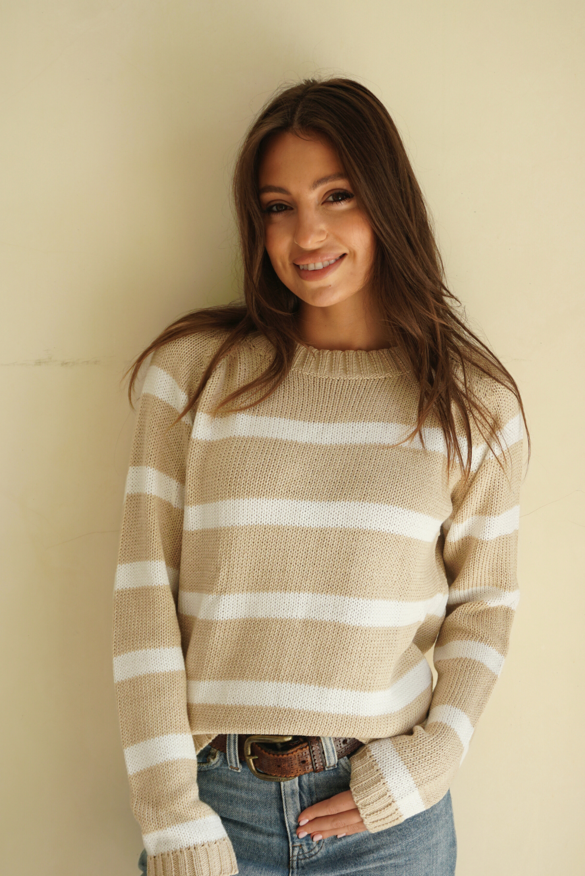 Soft Tan and Creamy Off-White Striped sustainable cotton handknitted Sloane Crewneck by Paneros Clothing. Relaxed-fit hip-length crewneck sweater with long sleeves and ribbing details. Front View tucked into denim.