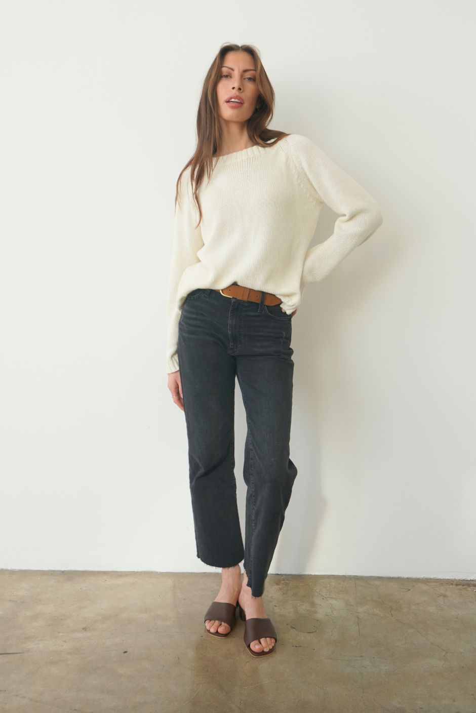 Creamy Off-White sustainable cotton handknitted Sloane Crewneck by Paneros Clothing. Relaxed-fit hip-length crewneck sweater with long sleeves and ribbing details. Front View tucked into denim.