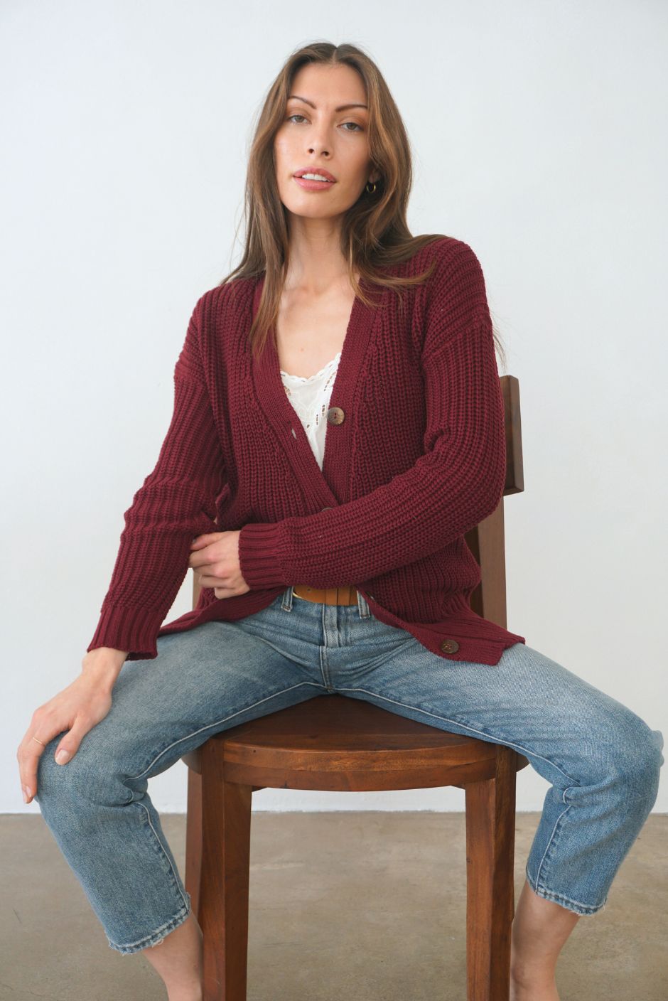 Burgundy Sustainable Cotton Hip-Length Button-up Emily Cardigan by Paneros Clothing. Hand-knitted, slightly oversized cardigan with real coconut shell buttons and ribbed detailing. Front View half-buttoned.