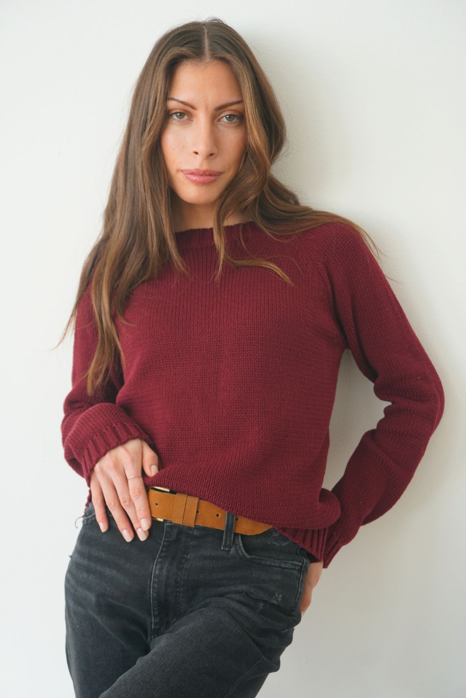 Burgundy sustainable cotton handknitted Sloane Crewneck by Paneros Clothing. Relaxed-fit hip-length crewneck sweater with long sleeves and ribbing details. Front View tucked into denim.