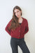 Burgundy sustainable cropped-length Cotton Diana Cardigan from Paneros Clothing with real coconut shell button-up front, Full sleeves, and feminine handknittting. Front View buttoned.