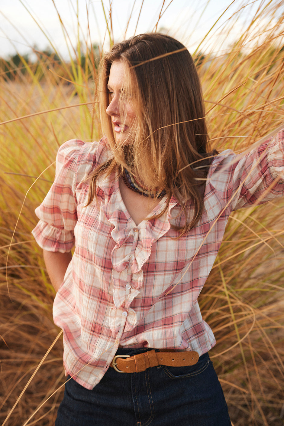 Woman in a pink plaid shirt with ruffles standing in tall grass