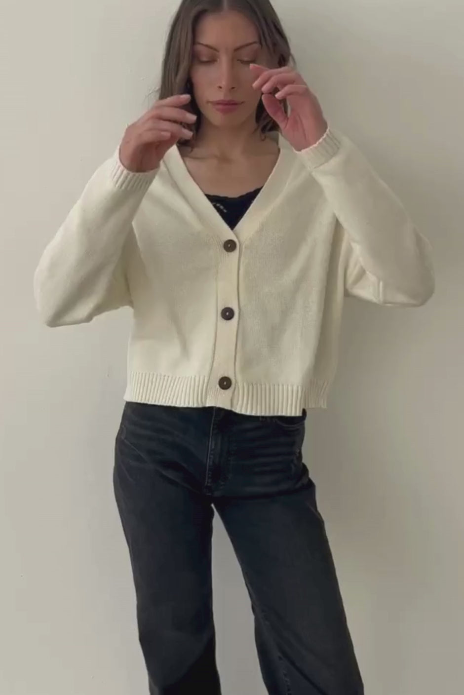 Creamy Off-White sustainable cropped-length Cotton Diana Cardigan from Paneros Clothing with real coconut shell button-up front, Full sleeves, and feminine handknittting. Full Body View in Motion, buttoned.