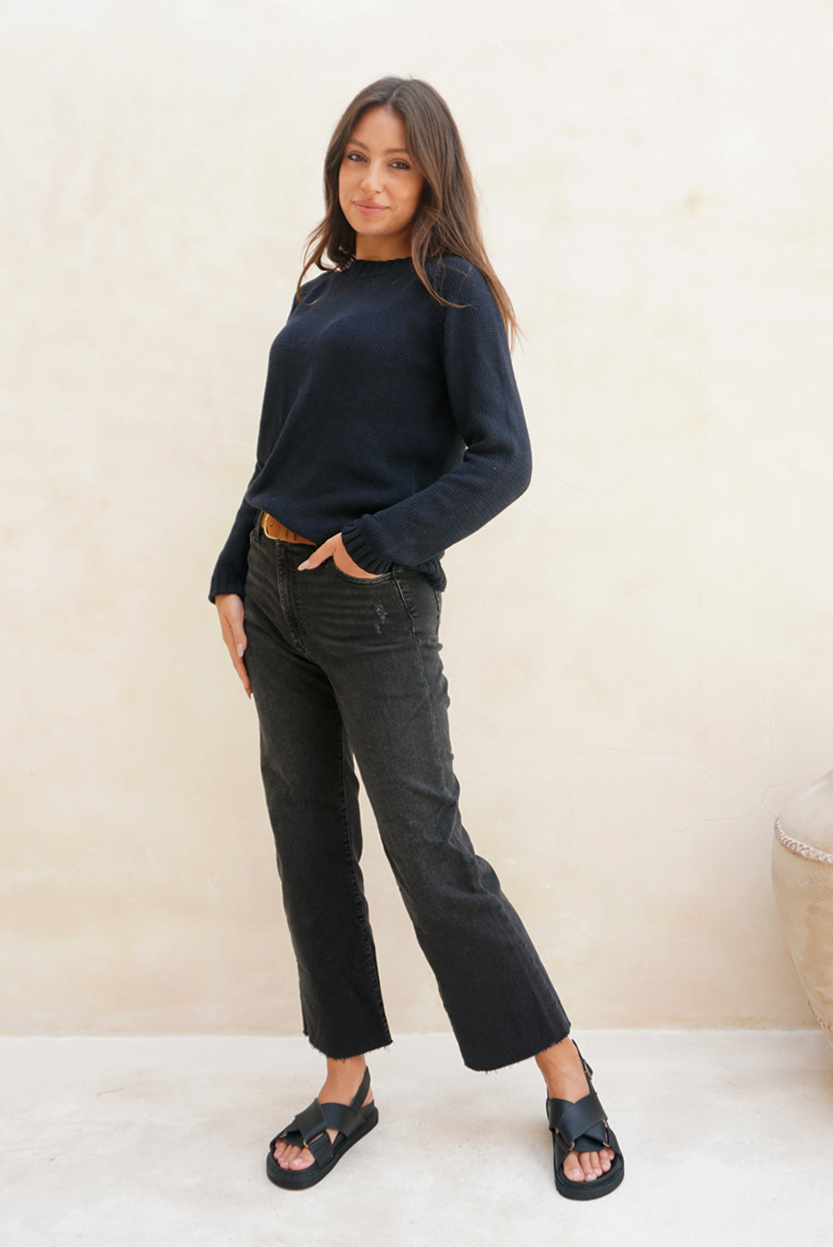 Navy Blue sustainable cotton handknitted Sloane Crewneck by Paneros Clothing. Relaxed-fit hip-length crewneck sweater with long sleeves and ribbing details. Front/Side View tucked into denim.