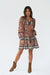 Brown Floral Print Long Sleeve Women's Sierra Above-the-Knee Mini Dress from Paneros Clothing with 100% certified sustainable fabric and smocking. Front View styled with boots and hand in pocket.