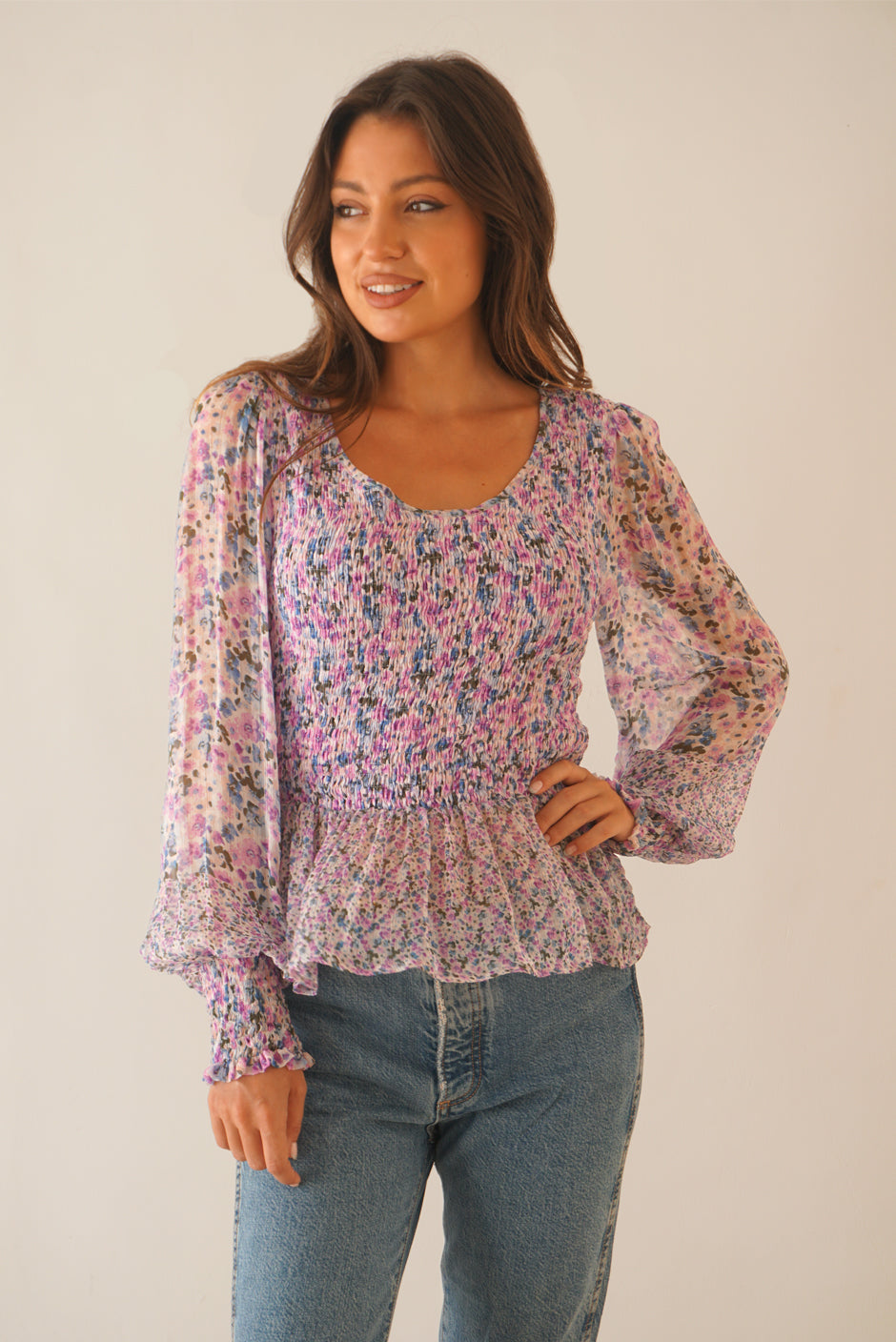 Purple Pink Floral Print Blouse Top for Women with smocking, ruffle details, and full length sleeves from Paneros Clothing: the Stella Top. Front View untucked with hand on hip showing flowy arm details.